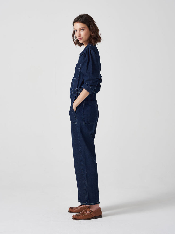 Relaxed fitting dark indigo washed denim Seventy + Mochi jumpsuit, gathered at the back, slightly cropped straight leg, and contrast stitching. Collagerie.com