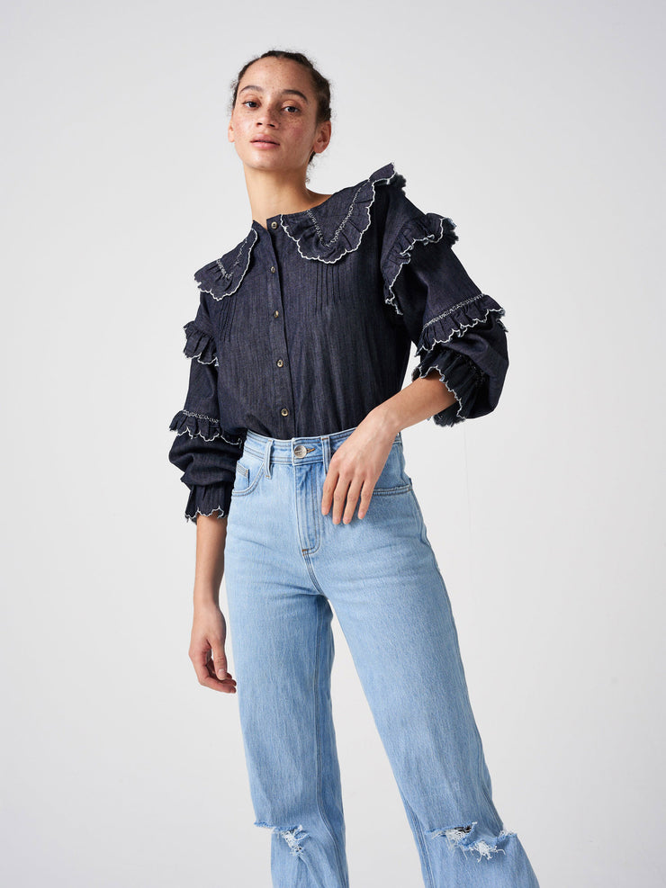 An all-season Seventy + Mochi blouse with scalloped frill detailing and soft balloon-shaped sleeves in washed indigo. Made from organic cotton. Collagerie.com